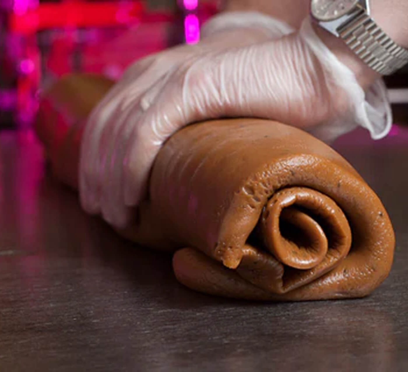 Hand wearing a glove holding a rolled piece of caramel on a reflective surface.

